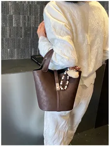Borsa a secchiello in pelle marrone con ciondolo orso e cinturino di perle, perfetto accessorio quotidiano.
