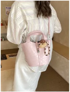 Primo piano della borsa a secchiello rosa con ciondolo a orsetto e design elegante.