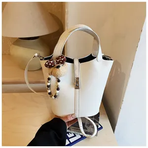 Vista dettagliata di una borsa a secchiello bianca con ciondolo a orsetto e cinturino di perle.
