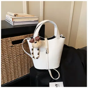 Borsa a secchiello bianca in pelle con dettaglio di ciondolo orsetto e tracolla chic.