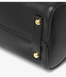 Close-up detail of black pebbled leather handbag featuring gold tone hardware rivets.