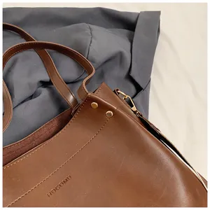Brown leather tote bag detail showing texture, metal hardware and double handles for casual use.