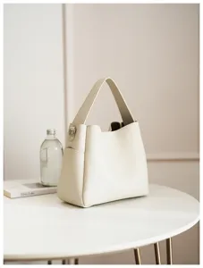 Detail view of the elegant beige pebbled leather bucket bag on a minimalist white table.