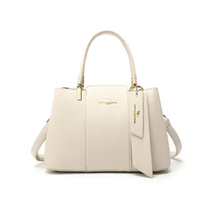 Élégant sac à main blanc cassé texturé en cuir avec poignées et pendentif chic.
