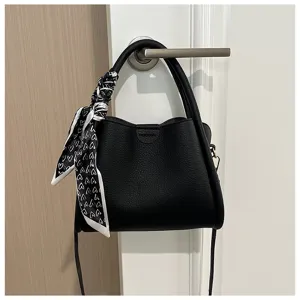 Detail shot of stylish black PU leather crossbody bag with cute heart scarf handle decoration.