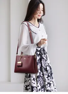 Wine red soft leather handbag detail, showing exquisite metal hardware and adjustable strap.