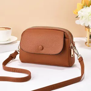Sac bandoulière en cuir marron pour femme, double fermeture éclair et rabat avec sangle réglable.