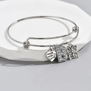 Adjustable silver tone bangle bracelet detail with rhinestone letter B and heart charm.