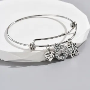 Detail view of silver adjustable wire bracelet with rhinestone letter G, heart and butterfly charms.