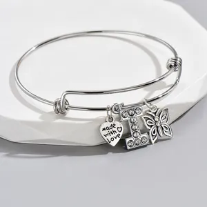 Close-up of silver wire bangle bracelet featuring rhinestone letter I, heart and butterfly charms.