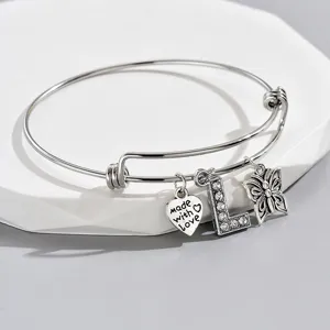 Close-up detail of silver adjustable bangle bracelet with love, letter L, and butterfly charms.