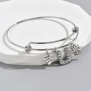 Close-up detail of adjustable silver wire bangle with rhinestone letter U and butterfly charms.