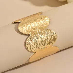 Ancho brazalete dorado martillado con motivos de trébol de cuatro hojas, joya elegante.
