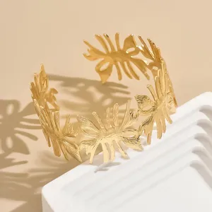 Bracciale rigido aperto dorato con trama a foglie cave intricate, elegante gioiello da donna.