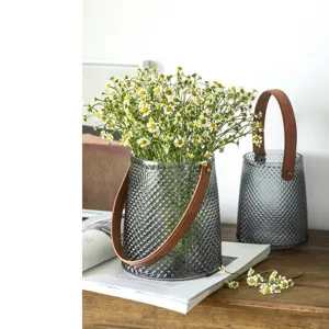 Transparent glass vase with leather handle and flowers, modern decorative centerpiece for home.
