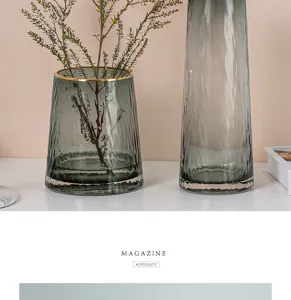 Detailed shot of transparent gray-green glass vases with gold rims and green plants.