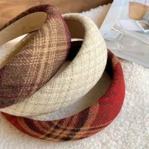 Close-up view of three thick plaid and tweed headbands layered on soft white plush background.