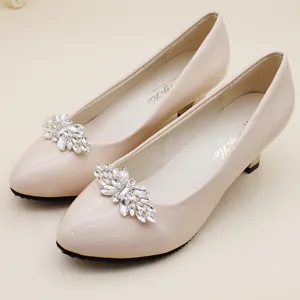 Primer plano de tacones de charol beige con clips para zapatos de flores de cristal brillante.