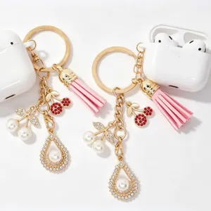 Detailed view of gold metal keychain with pink tassel, pearl cherries, and rhinestone charm.