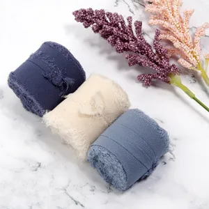Nahaufnahme von ausgefransten Chiffonband-Rollen in Blau und Beige auf Marmor-Hintergrund.