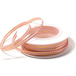 Detailed close-up of pink polyester ribbon featuring shiny gold edges wound neatly on a white spool.