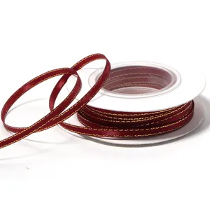 Close-up detail of the burgundy ribbon roll with metallic gold edge, showing fine texture.
