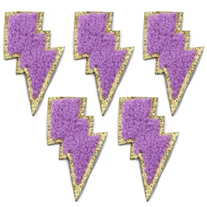 Primo piano di toppe a fulmine in ricamo spugna viola con bordi glitterati oro lucido.