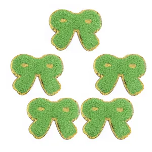 Dettaglio toppa in tessuto fiocco ricamo spugna verde bordo oro, perfetto per decorare vestiti fai da te.