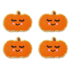 Dettaglio di quattro toppe ricamate a zucca arancione con rifinitura in glitter dorato.