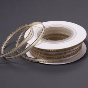 Close up detail view of white polyester ribbon featuring sparkling gold edges on spool.