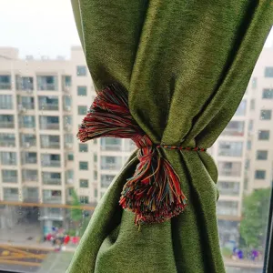 Detail shot of a bohemian multi-colored tassel curtain tieback hanging on a green curtain.