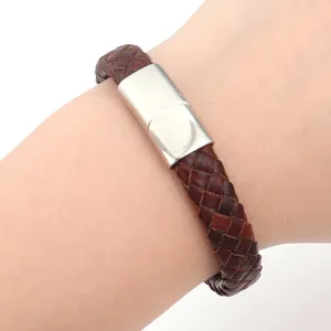 Gedetailleerde close-up van bruine gevlochten lederen armband met roestvrijstalen magneetsluiting.