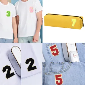 Dettaglio toppa termoadesiva numero in ciniglia ricamata con bordo oro su vestiti e borse.