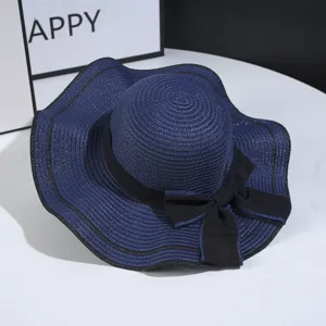 Close up of navy blue straw hat with black bow and wavy brim, perfect for summer sun protection.