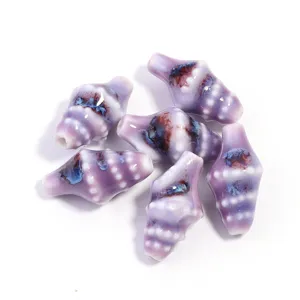 Close-up of handmade ceramic conch shaped beads with purple glaze and unique blue brown patterns.