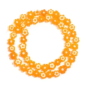 Close-up detail of orange and white flower glass beads strand for DIY jewelry making.