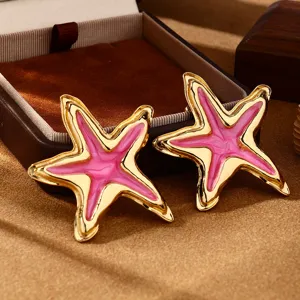 Primo piano dettagliato di orecchini a stella Marina dorati con smalto rosa brillante.