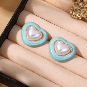 Detailaufnahme von trendigen kontrastfarbenen Herz-Ohrringen mit Perle und hellblauer Kante.