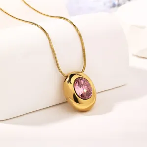 Close-up detail of a gold oval pendant necklace sparkling with a delicate pink cubic zirconia.