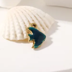 Primo piano del piccolo ciondolo a forma di pesce in smalto blu, metallo lucido, sfondo di conchiglia.