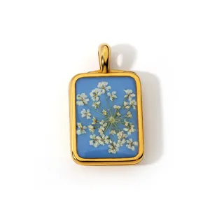 Gedetailleerd shot van een rechthoekige hars hanger met witte gedroogde bloemen op blauw.