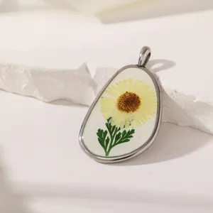 Gedetailleerde close-up van hars hanger met gedroogde bloem en zilverkleurig frame.