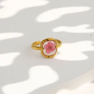 Close-up of gold-plated stainless steel ring featuring transparent pink preserved flower detail.