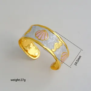 Detail shot of gold-plated open cuff bracelet with white pink enamel shell seahorse design.