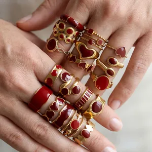 Close-up detail of stacking wine red enamel rings on fingers, stainless steel gold finish.