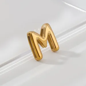 Golden letter M pendant accessory, polished stainless steel surface, elegant minimalist detail.