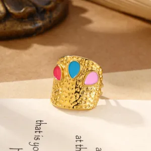 Detailopname van een brede gouden roestvrijstalen ring met kleurrijke emaillen stenen.