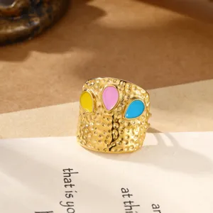 Close-up detail van brede gouden roestvrijstalen gehamerde ring met kleurrijke druppels.