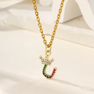 Primo piano dettagliato di una collana con ciondolo a lettera e corona con zirconi colorati.