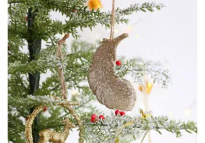 Ornement de sapin de Noël gros plan, détail de plume et cerf pailleté or étincelant.